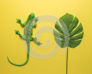 Green lizard toy with palm leaf on bright yellow background. Minimal art concept