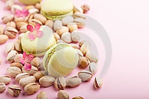 Green macarons or macaroons cakes with pistache nuts on pastel pink background. side view, copy space