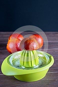 The green manual juicer on the table is prepared for squeezing juice from red Sicilian orange