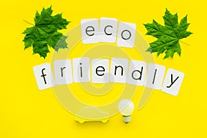 Green maple leaves, car figure, bulb and eco friendly text for ecology concept on yellow background top view