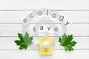 Green maple leaves, house figure, bulb and ecology save text for eco concept on white wooden background top view