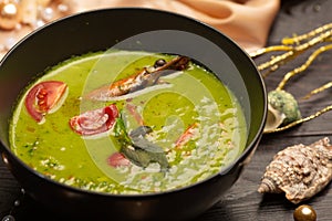 Green mashed soup with spinach and shrimp in a black plate