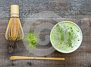 Green matcha latte drink and tea accessories on wooden table top view.