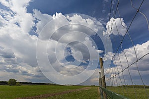 Green meadow with country road, clouds and fence on foreground