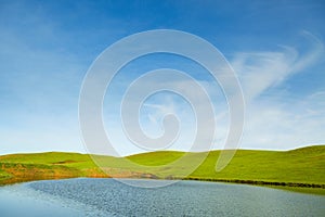 Green meadow with lake, hills and sky