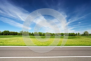 Green meadow with trees and asphalt road