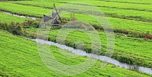 Green meadow on water canals and Dutch traditional small wooden windmill