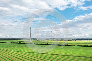 Green meadow with wind turbines generating electricity, summer landscape with blue sky, alternative energy sources