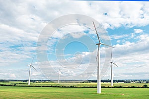 Green meadow with wind turbines generating electricity, summer landscape with blue sky, alternative energy sources