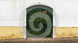 Green metal door with a white and yellow house front on a cobblestone street