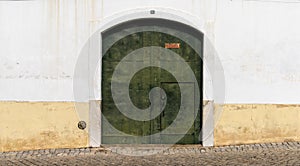 Green metal door with a white and yellow house front on a cobblestone street