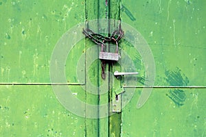 Green metal doors with cracked paint and dilapidated door handle locked with rusted chain and old padlock