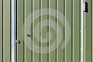 Green metal fence and doors made of corrugated steel sheet with vertical rails and a surveillance camera