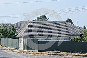 green metal fence wall in front of a house with a gray slate roof on the street