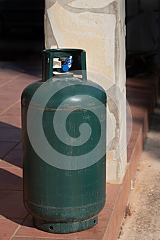 A green metal gas bottle stands on a terrace in Italy. It is a deposit bottle that should be refilled