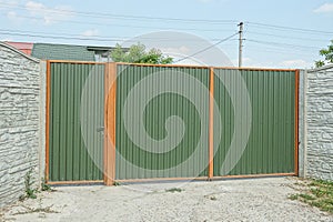 Green metal gate and closed door with part of gray concrete fence wall