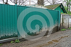 Green metal gate and a fragment of a fence on a rural street