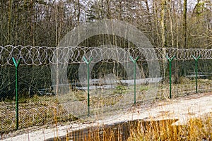 A green metal mesh fence with coiled barbed wire around the restricted area of a military facility
