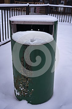 Green metallic trash can covered in snow