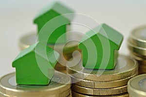 Green miniature houses on coin stacks - Concept of real estate investment, mortgage, home insurance and loan, eco-friendly house