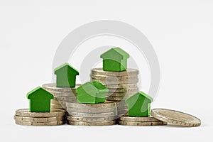 Green miniature houses on coin stacks on white background - Concept of real estate investment, mortgage, home insurance and loan,