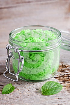 Green mint scrub in a glass jar and fresh spearmint leaves. Natural beauty treatment and spa recipe.