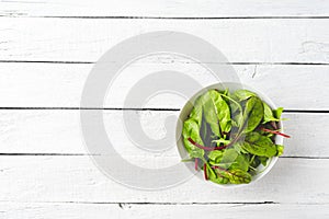 Green mixed salad with spinach, arugula and beetroot leaves in bowl on white wooden table with copyspace.