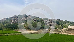 Green mountain filled with rocks adjacent to agriculture area photo