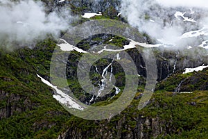 Green mountain slope with snow and waterfalls