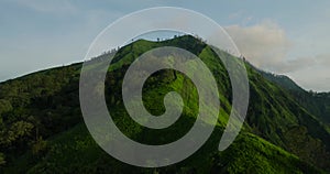 Green mountain with trees under cloudy sky seen from above