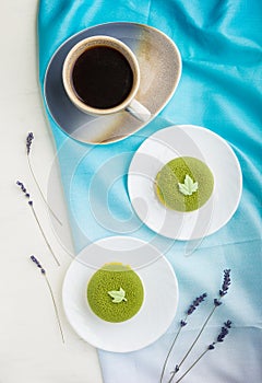Green mousse cake with pistachio cream and a cup of coffee on a white wooden background. top view, close up