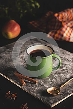 In a green mug on a black background hot mulled wine from red wine with the addition of apple and cinnamon.