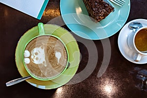 Coffee latte art on drown wooden table top view. Latte hot coffee in a green cup with latte art served with piece of orange-