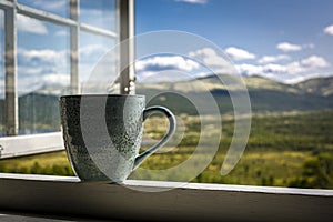 Green mug of coffee and mountain view through an open window