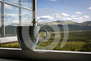 Green mug of coffee and mountain view through an open window