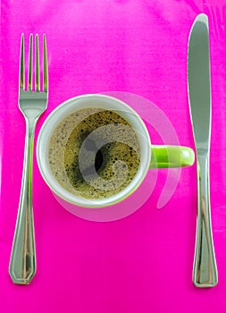 Green mug with coffee on saucer with cutlery.