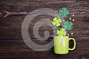 Green mug with four-leaf clover on wooden background. Copy space