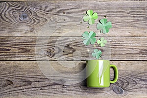 Green mug with four-leaf clover on wooden background. Copy space