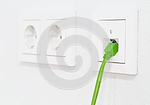 Green network cable in wall outlet for office or private home lan ethernet connection with power outlets flat view on white