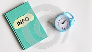 On a green notebook is a piece of paper with the word INFO on a white background next to the alarm clock.