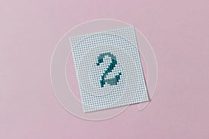 Green number 2 cross-stitch embroidered on piece of canvas in center of pink background. Hobbies, pastime, activity, art