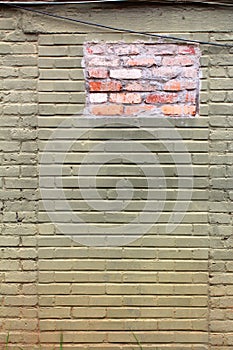 Green and ochre painted old brick wall with a patch of new brick