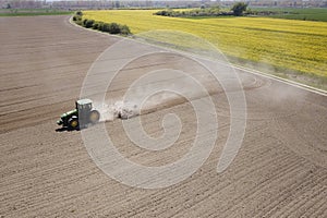 Green old tractor cultivates the dusty field with liner