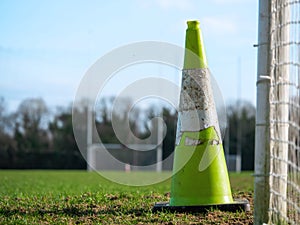 Green old weathered cone on a grass field. In the background tall goal post for Irish National sports camogie, hurling, rugby,