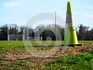 Green old weathered cone on a grass field. In the background tall goal post for Irish National sports camogie, hurling, rugby,