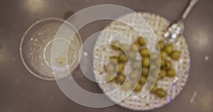 Green olive falls into glass of sparkling wine. Top view, close-up. A plate with olives on the background.