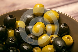 Green olives and black olives in a ceramic bowl on a wooden background. Close up