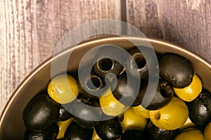 Green olives and black olives in a ceramic bowl on a wooden background. Close up