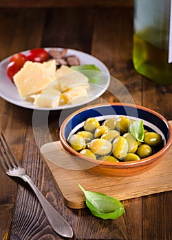 Green olives in a ceramic bowl on wooden background