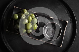 Green olives in a ceramic bowl on a wooden background.